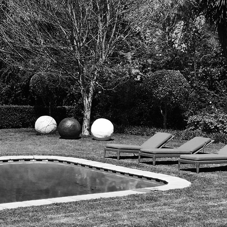 Three cement spheres in white and charcoal on a lawn beside a pool